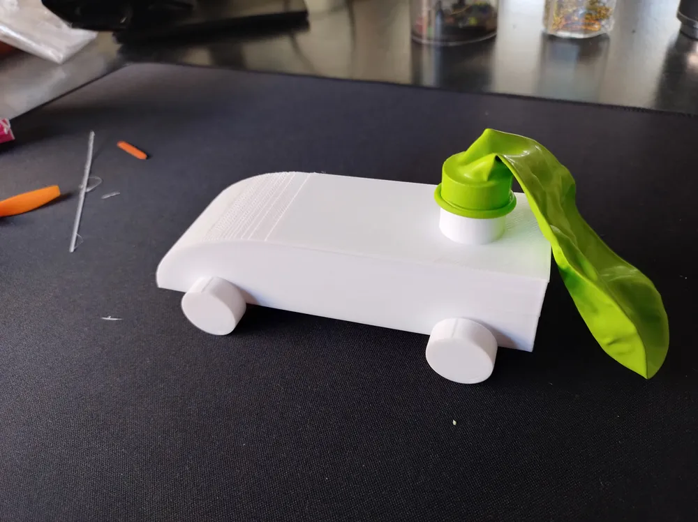 Auto a reacción impreso en 3D propulsado por un globo, sobre la mesa del taller.